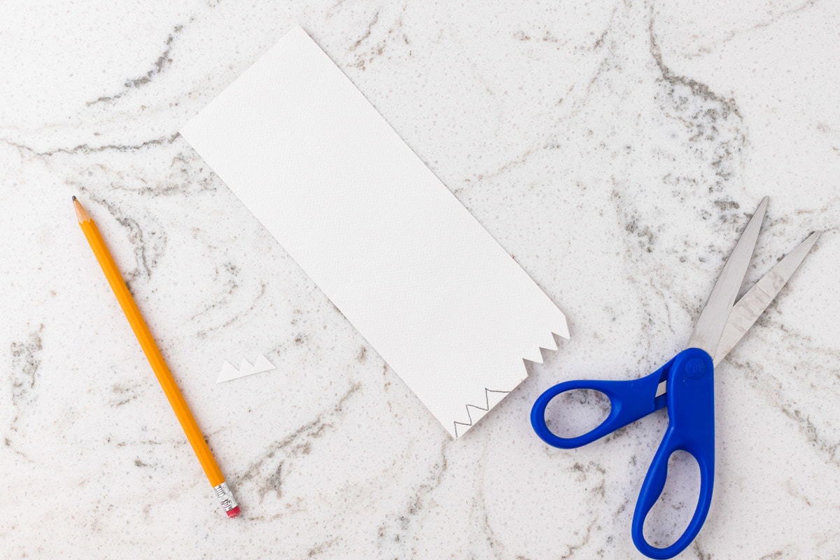 White cardstock with a zigzag edge being cut to create pointed monster teeth.