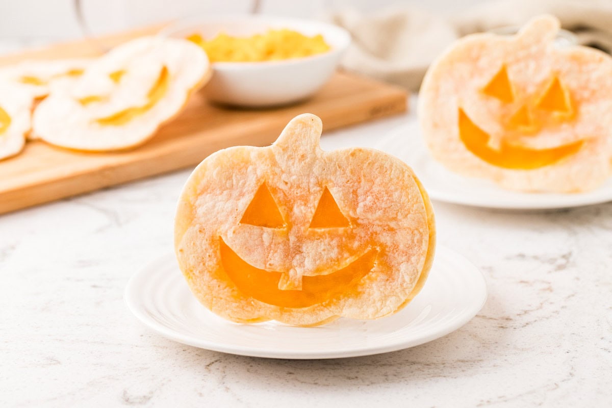 Pumpkin-shaped Halloween quesadilla with a smiling jack-o’-lantern face and melted cheddar cheese served on a white plate.